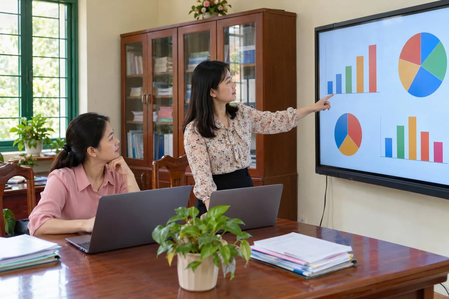 Giáo viên trao đổi trước màn hình tương tác hiển thị biểu đồ dữ liệu trong phòng hội đồng nhà trường
