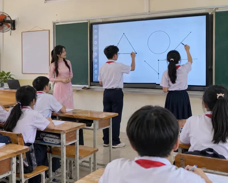 Cô giáo và hai học sinh THCS thao tác trên màn hình tương tác trong lớp học, các bạn khác ngồi theo dõi